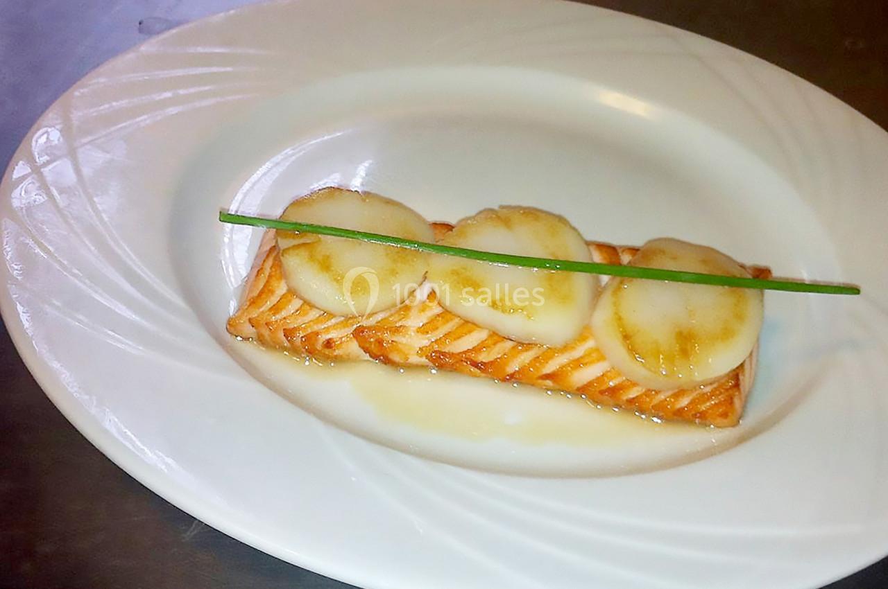Filet de saumon grillé garni de tranches de Saint-Jacques et d'une tige de ciboulette, présenté sur une assiette blanche.