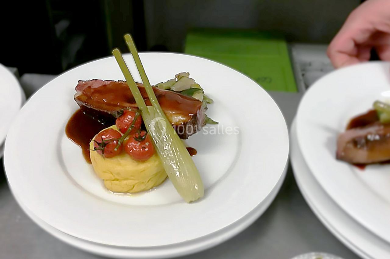 Assiette gastronomique avec viande nappée de sauce, purée, légumes grillés et oignon entier, servie sur une table.
