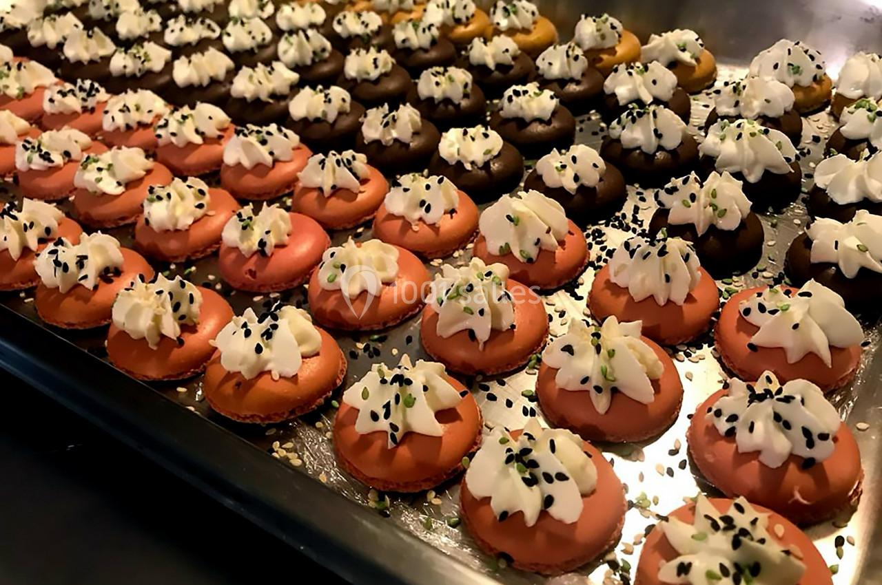 Plateau de petits gâteaux colorés garnis de crème fouettée et décorés de graines noires et vertes.