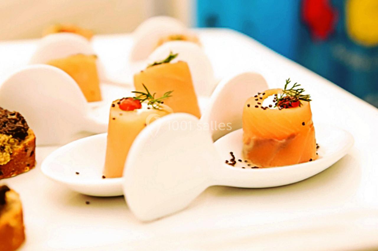 Bouchées de saumon fumé garnies de crème et d'aneth, présentées sur des cuillères blanches en porcelaine.