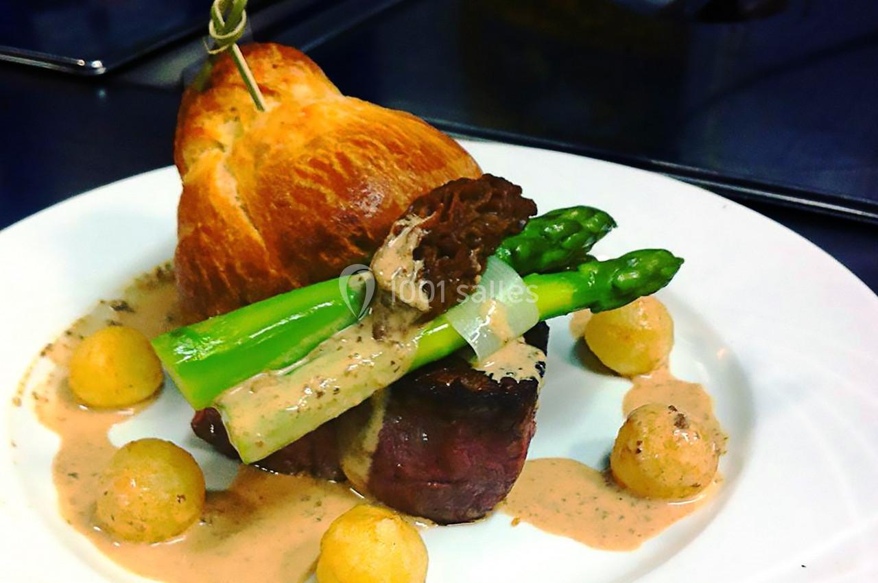 Assiette gastronomique avec filet de viande, asperges, morille, sauce crémeuse, pommes dauphines et brioche en arrière-plan.