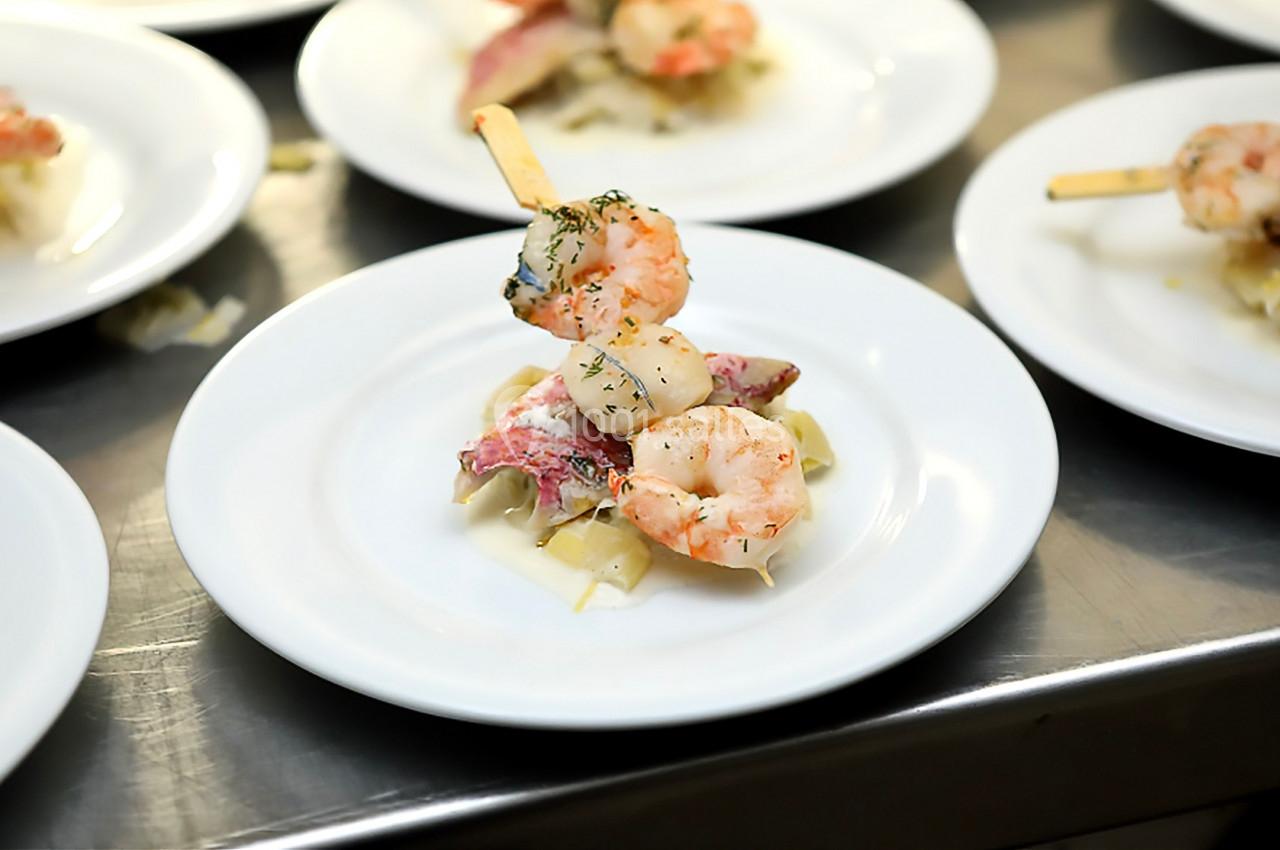 Brochette de crevettes et poisson sur un lit de pâtes, servie dans une assiette blanche.