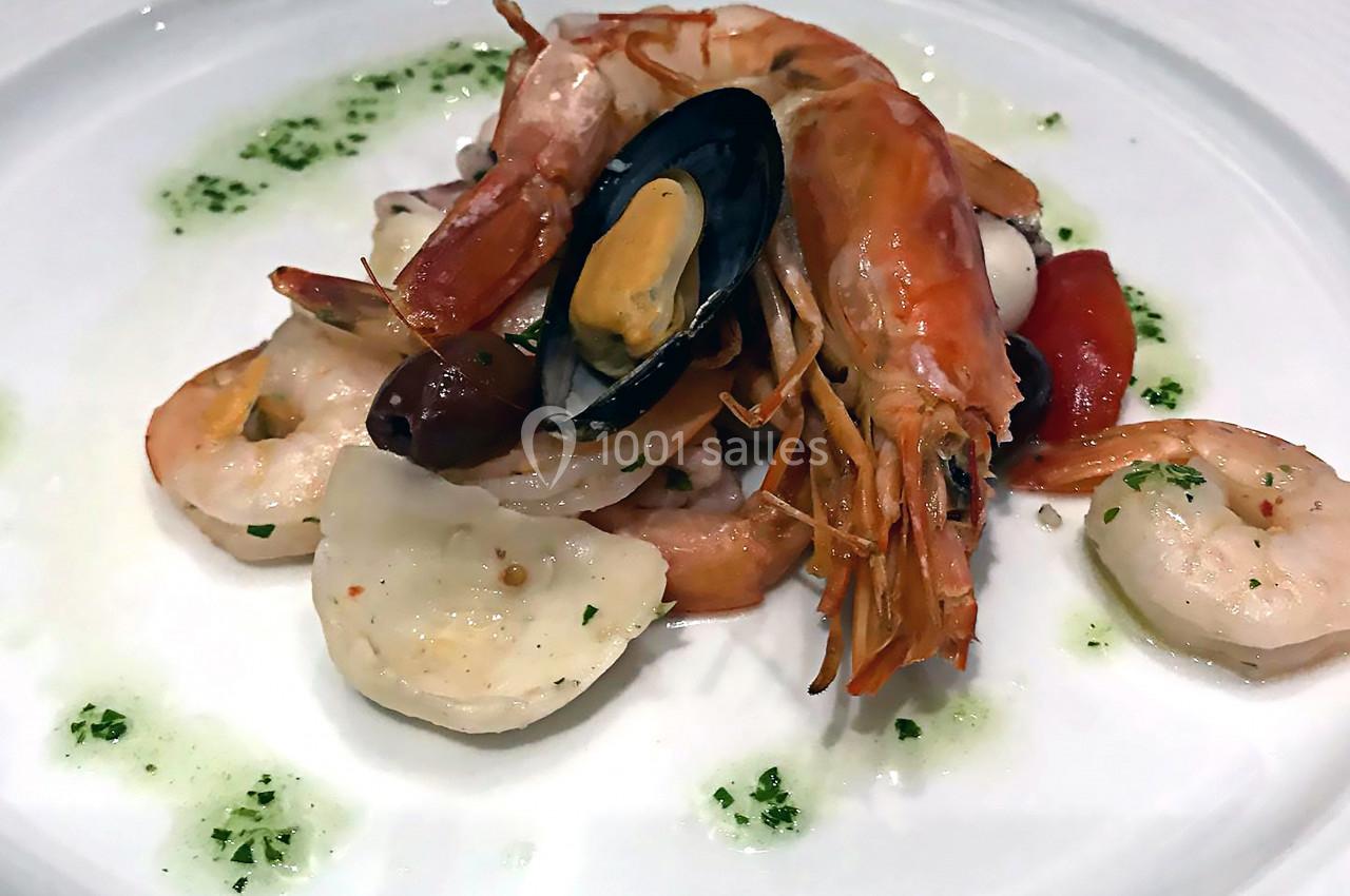 Assiette de fruits de mer variés avec crevettes, moules, calamars et tomates, accompagnés d'une sauce verte.