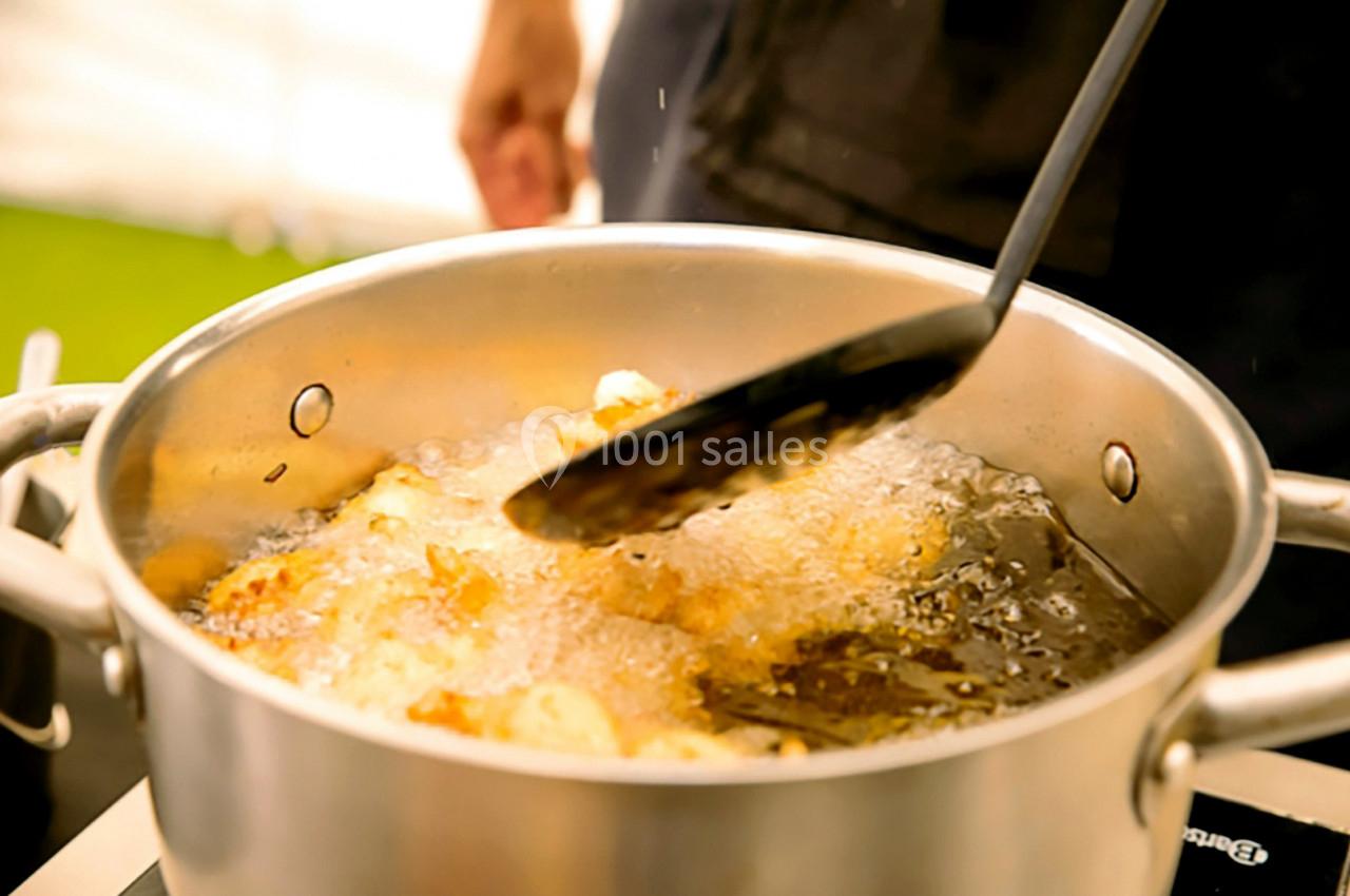 Cuisson de morceaux d'aliments dans une casserole d'huile bouillante, avec une écumoire en mouvement.