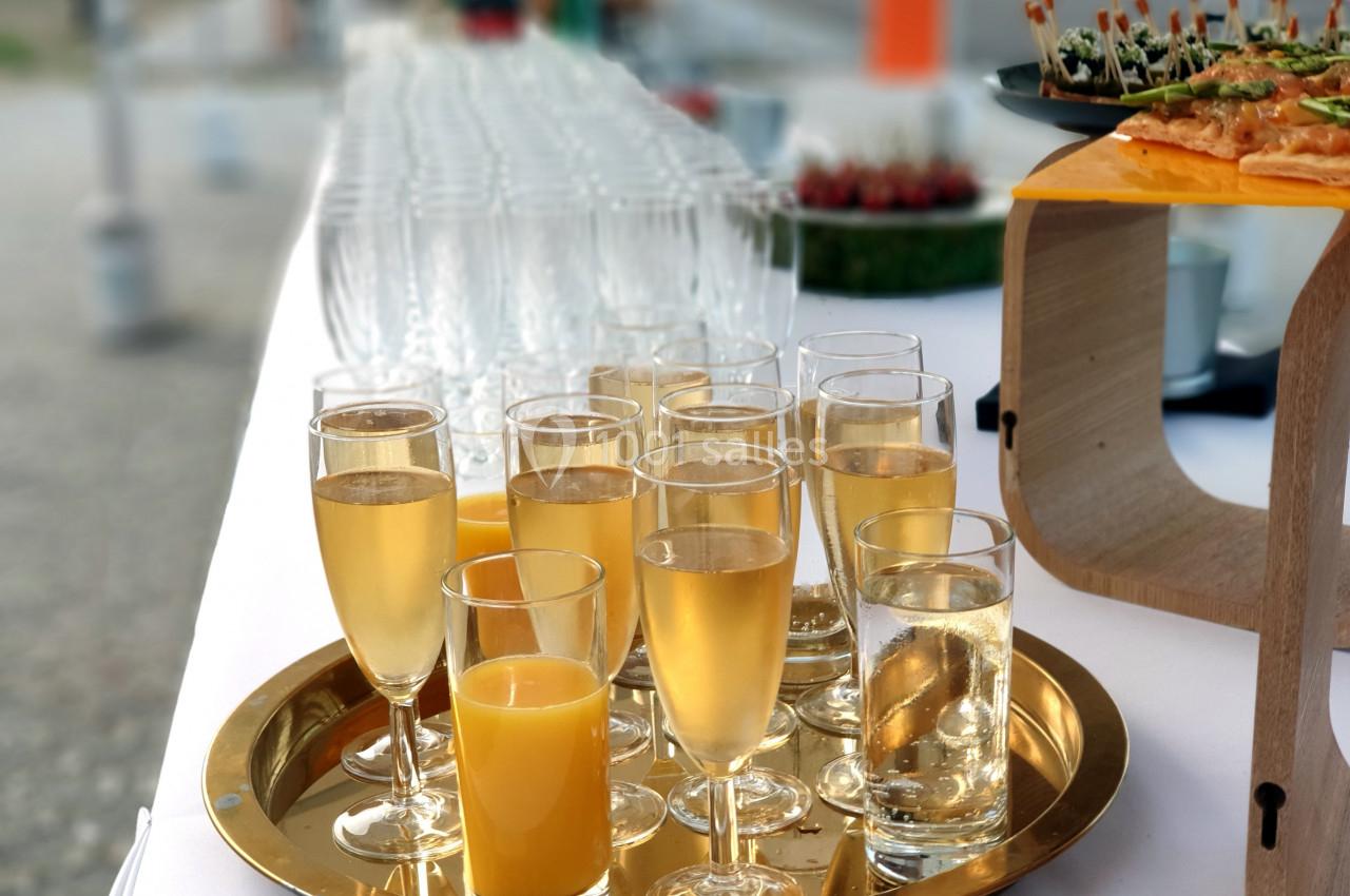 Plateau de verres remplis de boissons, incluant du jus d'orange et des bulles, sur une table dressée pour un événement.