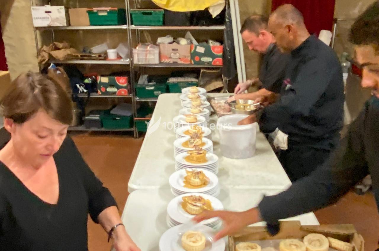 Des personnes préparent et dressent des assiettes avec des desserts dans une cuisine professionnelle.