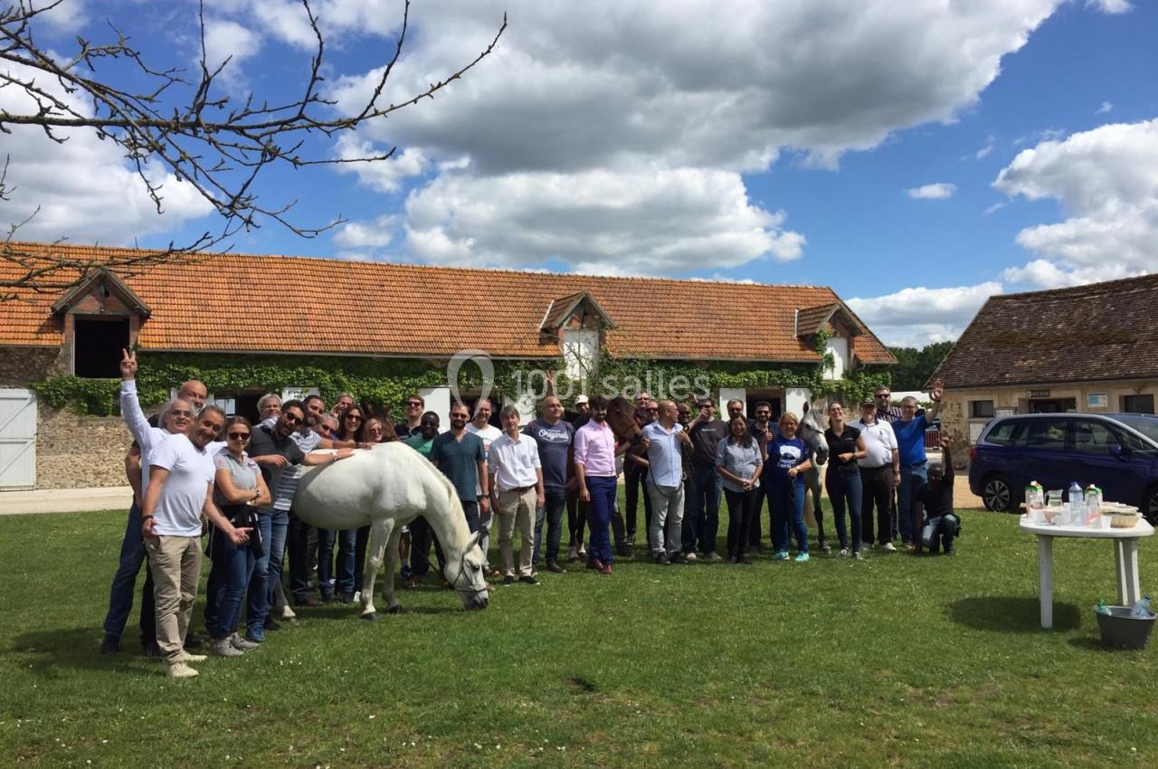 Un groupe de personnes rassemblées sur une pelouse devant des bâtiments en pierre, avec un cheval blanc au premier plan.