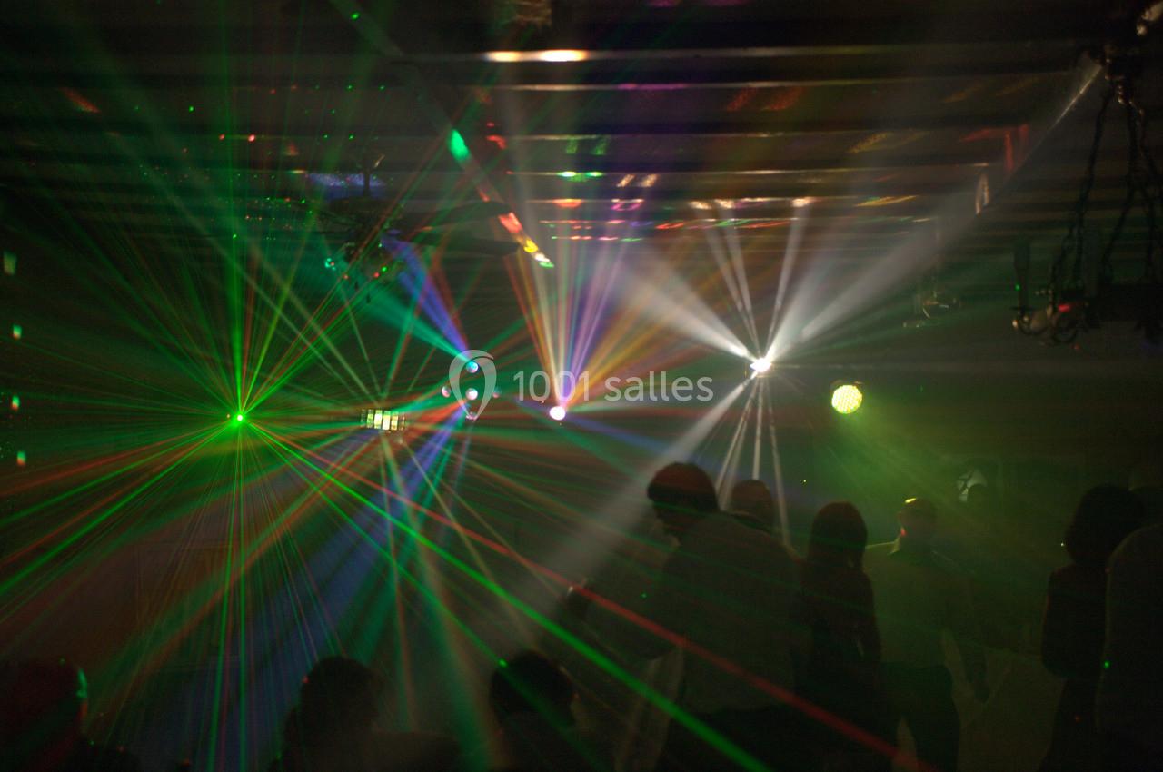 Jeux de lumières colorées et faisceaux laser éclairant une salle sombre avec des silhouettes de personnes.
