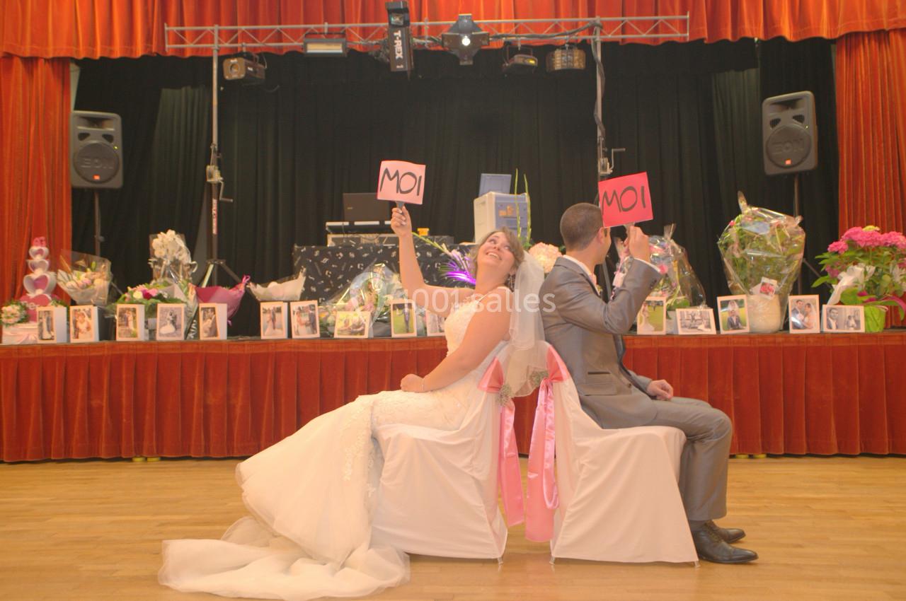 Un couple assis dos à dos lors d'une fête, tenant des pancartes ’MOI’, entouré de décorations et de fleurs.