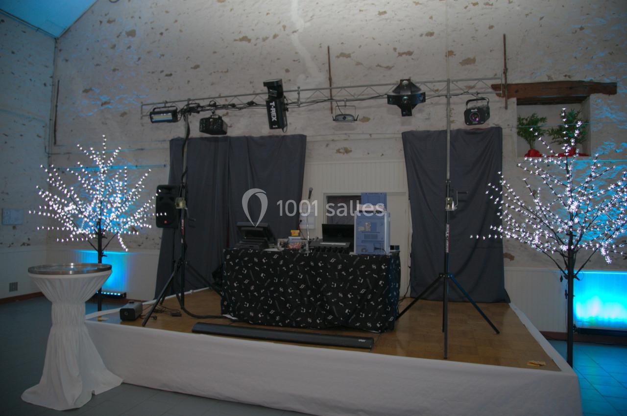 Scène de DJ installée dans une salle avec éclairages décoratifs et arbres lumineux en arrière-plan.