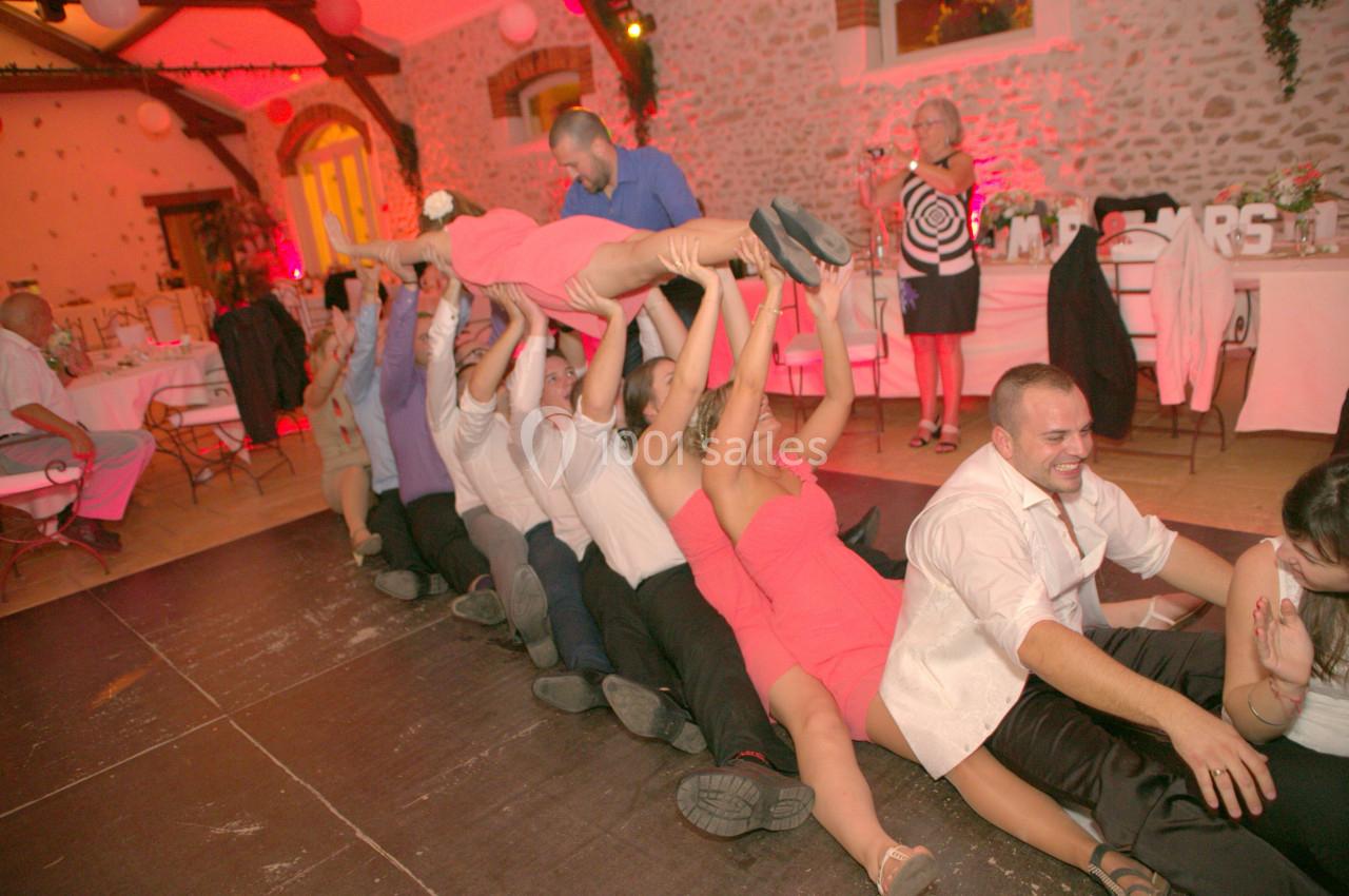 Des personnes assises en file indienne dans une salle de réception, portant une femme en robe rose au-dessus d'elles.