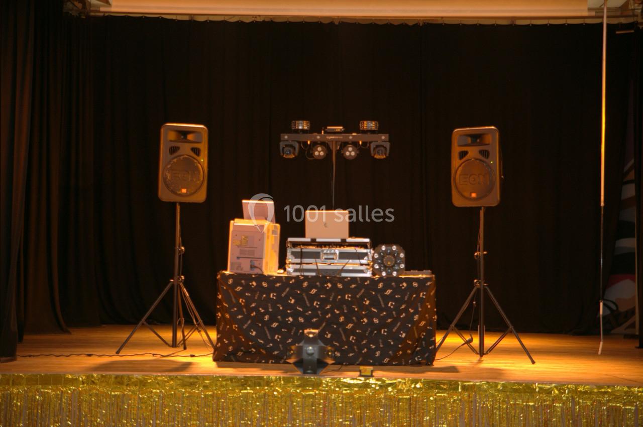 Table de DJ équipée de matériel audio et éclairage, installée sur une scène avec rideaux noirs en arrière-plan.