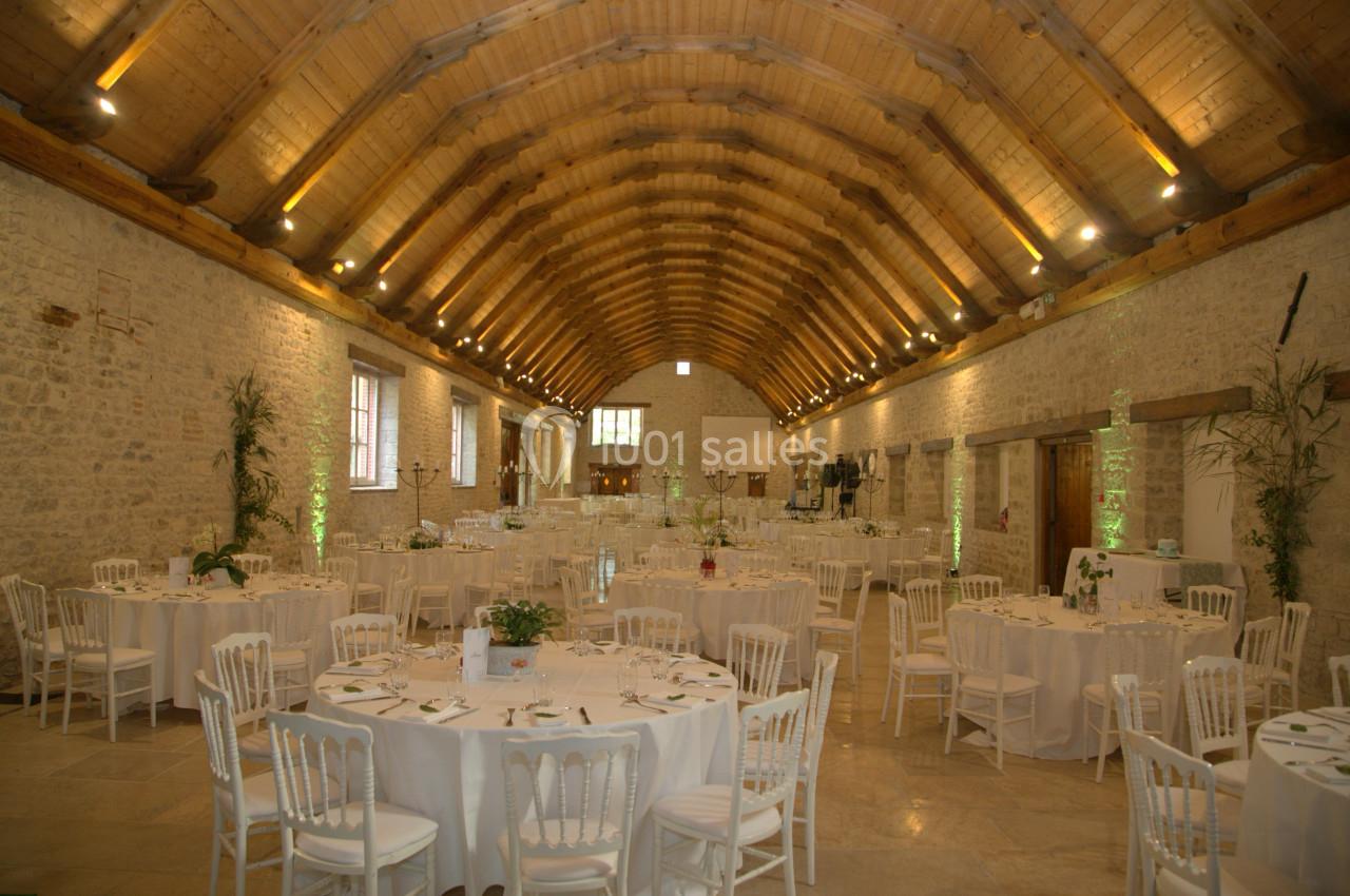 Salle de réception en pierre avec plafond voûté en bois, tables rondes dressées et éclairage chaleureux.