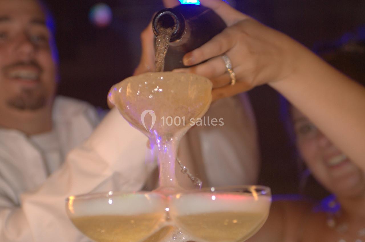 Deux personnes versent du champagne dans une pyramide de coupes, créant un effet de débordement festif.