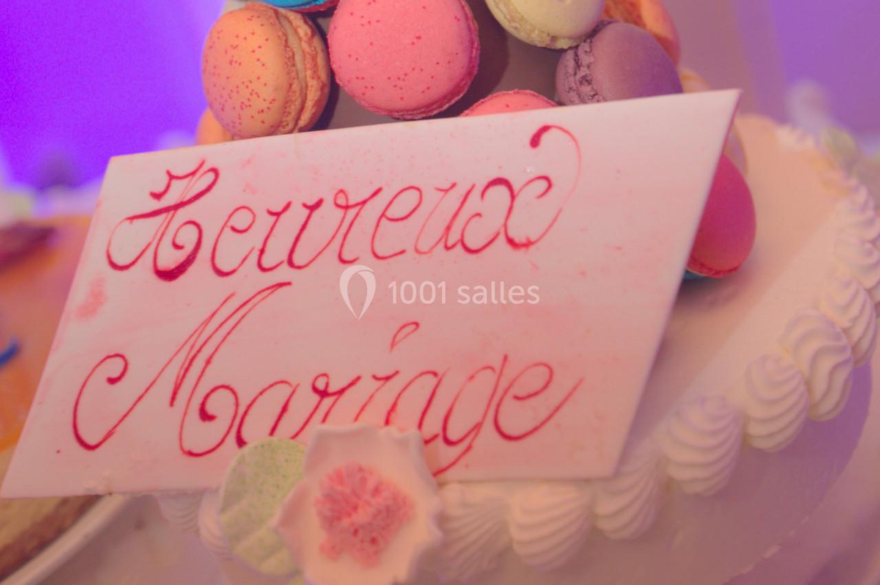 Plaque en sucre avec l'inscription ’Heureux Mariage’ posée sur un gâteau décoré de macarons colorés.
