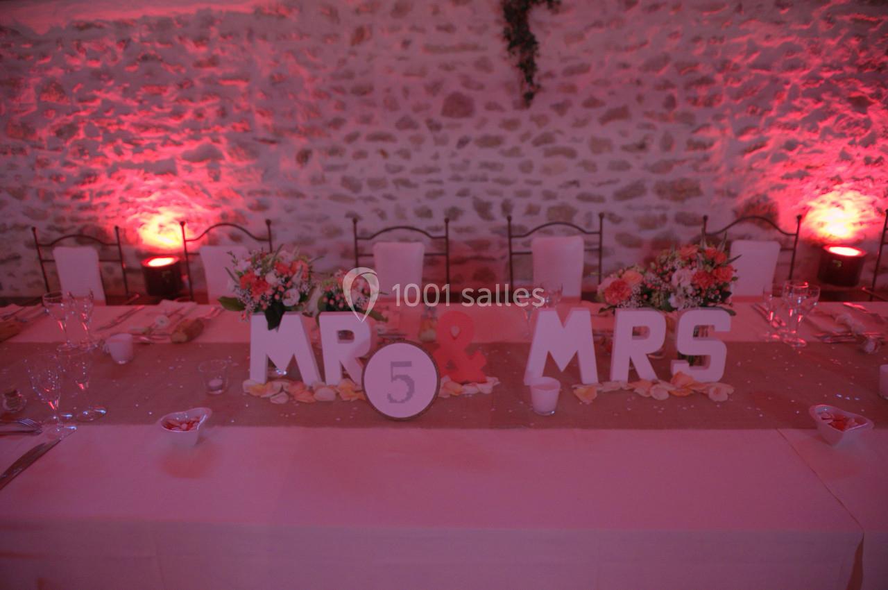 Table de mariage décorée avec des fleurs, des lettres ’MR & MRS’ et un chiffre 5, éclairée par une lumière rose.