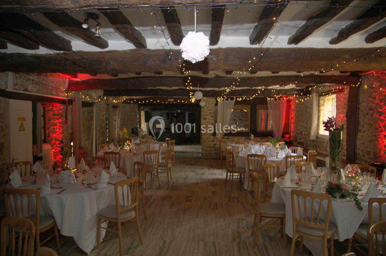 Salle de réception rustique décorée avec des guirlandes lumineuses, des tables rondes dressées et des murs en pierre…