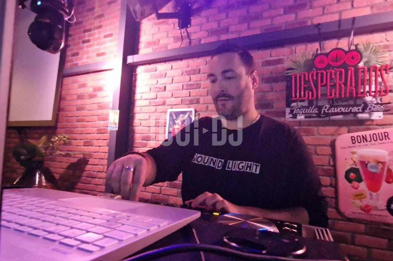 Un DJ mixe de la musique sur une console dans un bar à l'ambiance lumineuse et mur en briques.