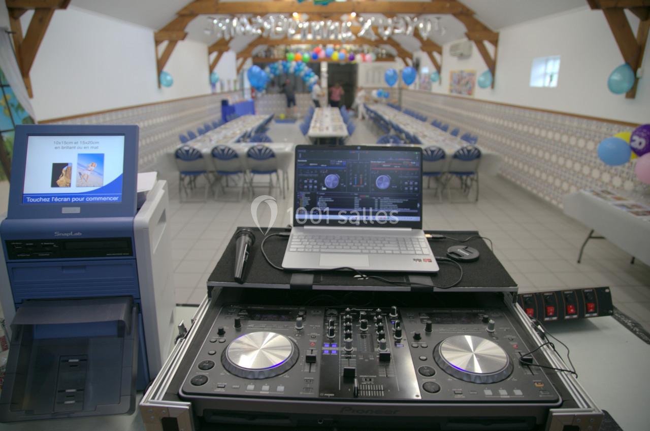 Table de mixage et ordinateur installés dans une salle décorée pour un événement avec tables alignées et ballons colorés.