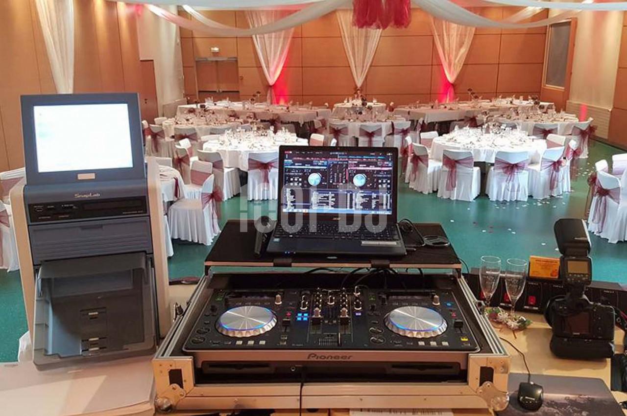 Table de mixage avec ordinateur et matériel DJ en premier plan, salle de réception décorée en arrière-plan.