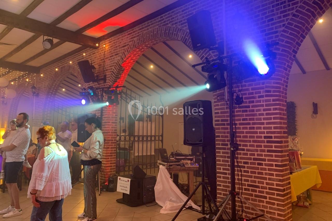 Salle de réception avec des invités debout, éclairages colorés et équipement de sonorisation près d'une arche en briques.