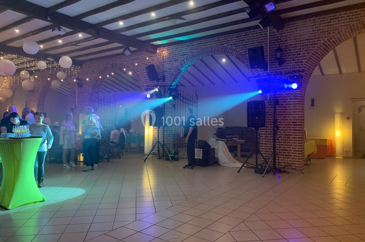 Salle de réception avec des invités debout, éclairages colorés et décorations suspendues.