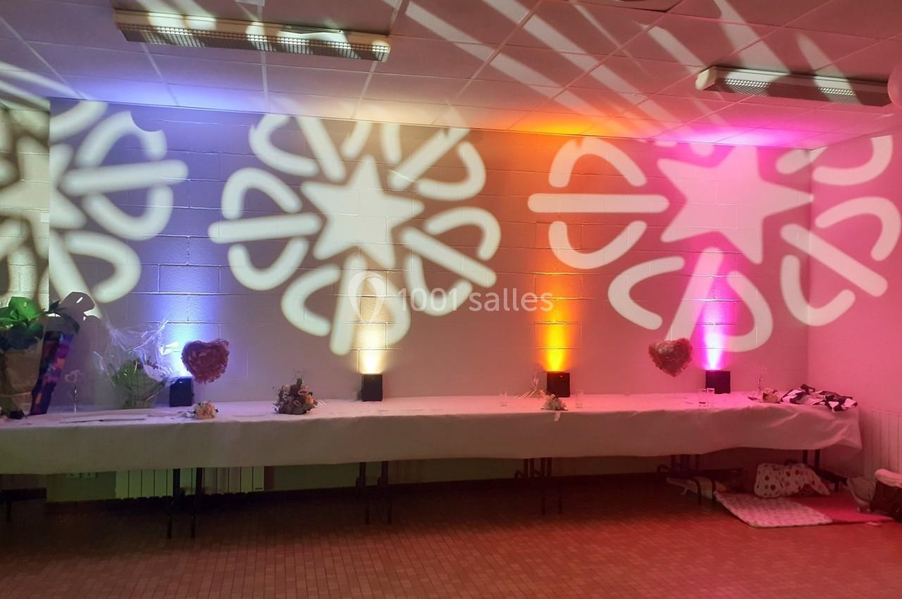 Salle décorée avec des projections lumineuses colorées en forme d'étoiles sur un mur blanc, table dressée en dessous.