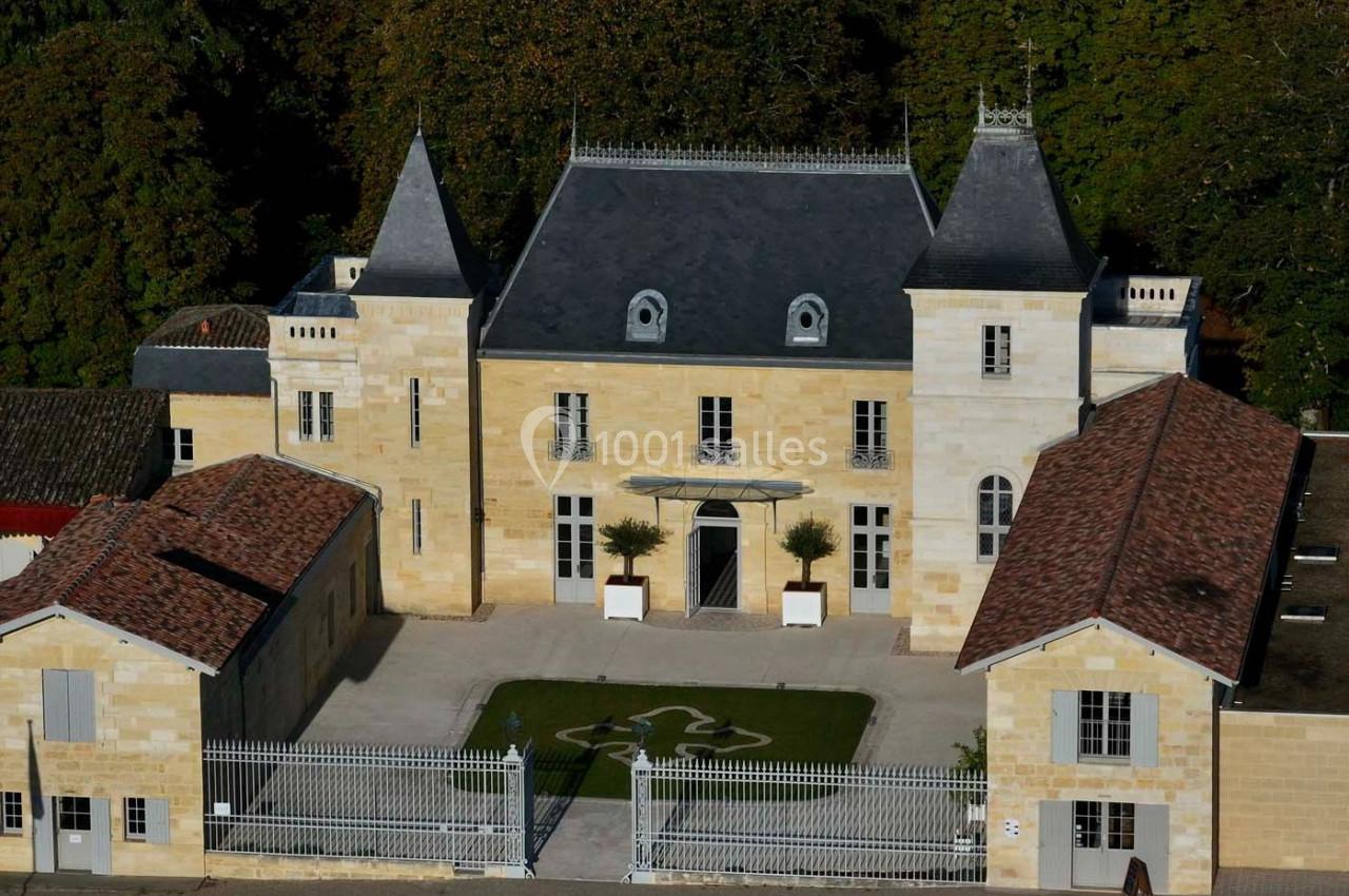 Façade d'un château en pierre avec deux tours, entouré de bâtiments annexes et d'une grille en fer forgé.