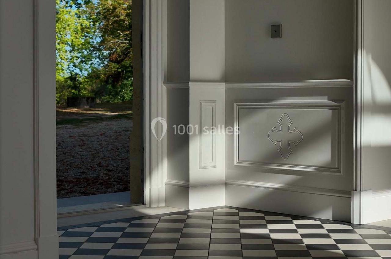 Sol en carrelage noir et blanc dans une pièce lumineuse, avec une porte ouverte donnant sur un espace extérieur arboré.