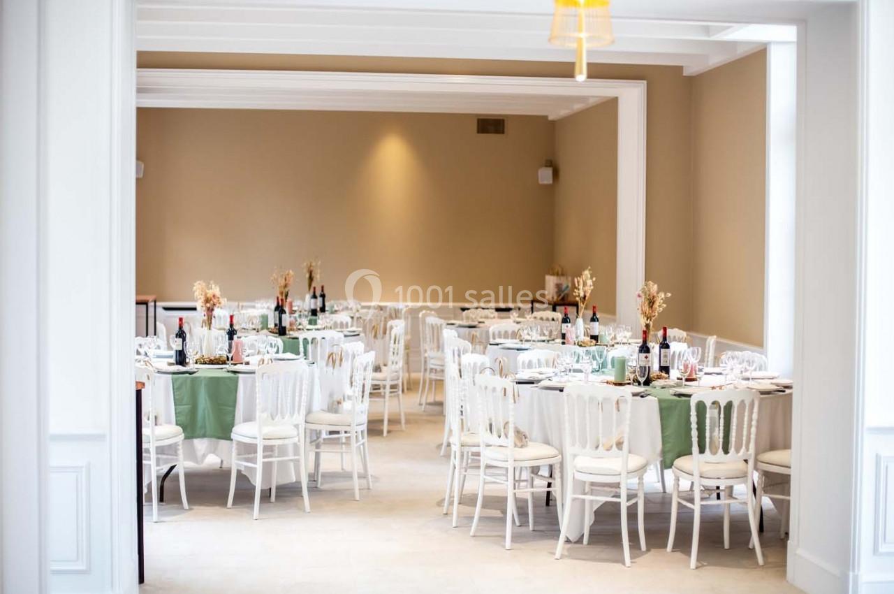 Salle de réception lumineuse avec des tables dressées, nappes vertes et blanches, et décorations florales.