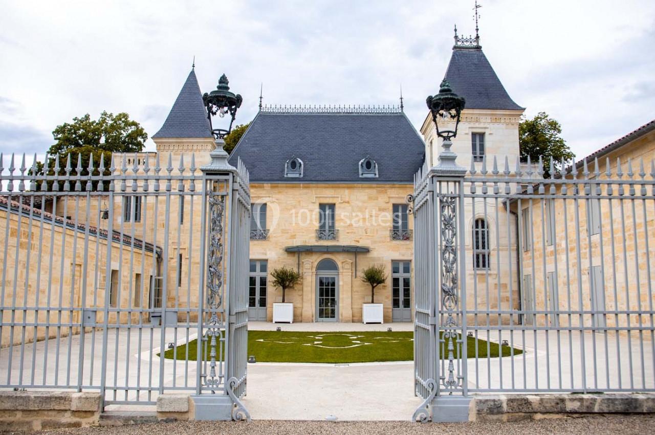Façade d'un château en pierre claire avec toit en ardoise, vue derrière une grille métallique ornée.