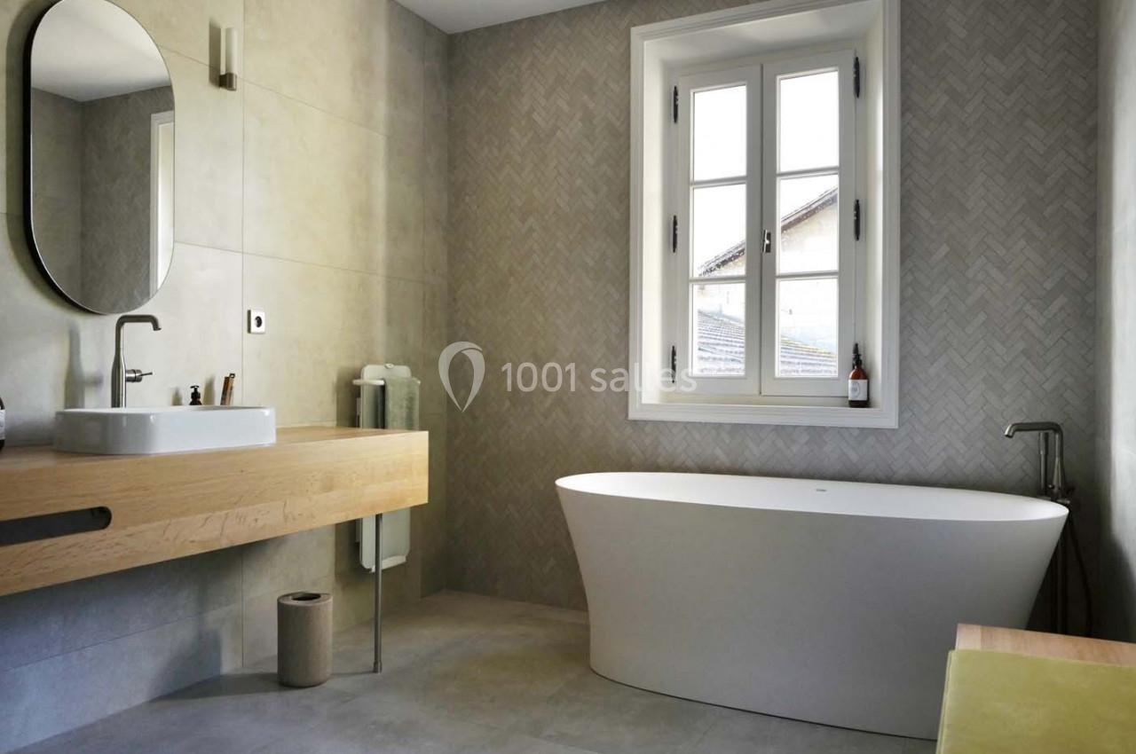Salle de bain moderne avec baignoire îlot, vasque sur meuble en bois clair et mur en carrelage à motif chevrons.