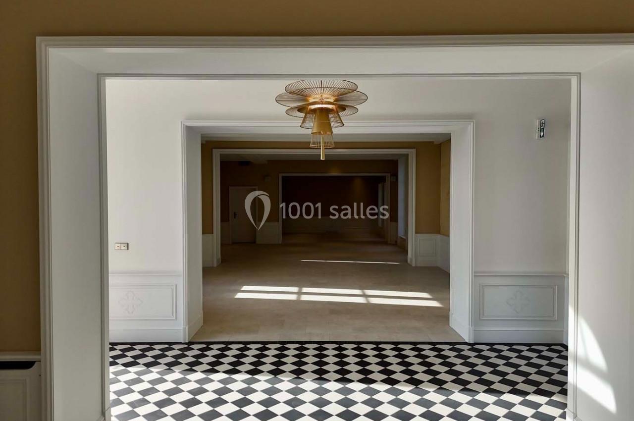 Vue d'un intérieur lumineux avec sol en damier noir et blanc, moulures blanches et lustre doré central.