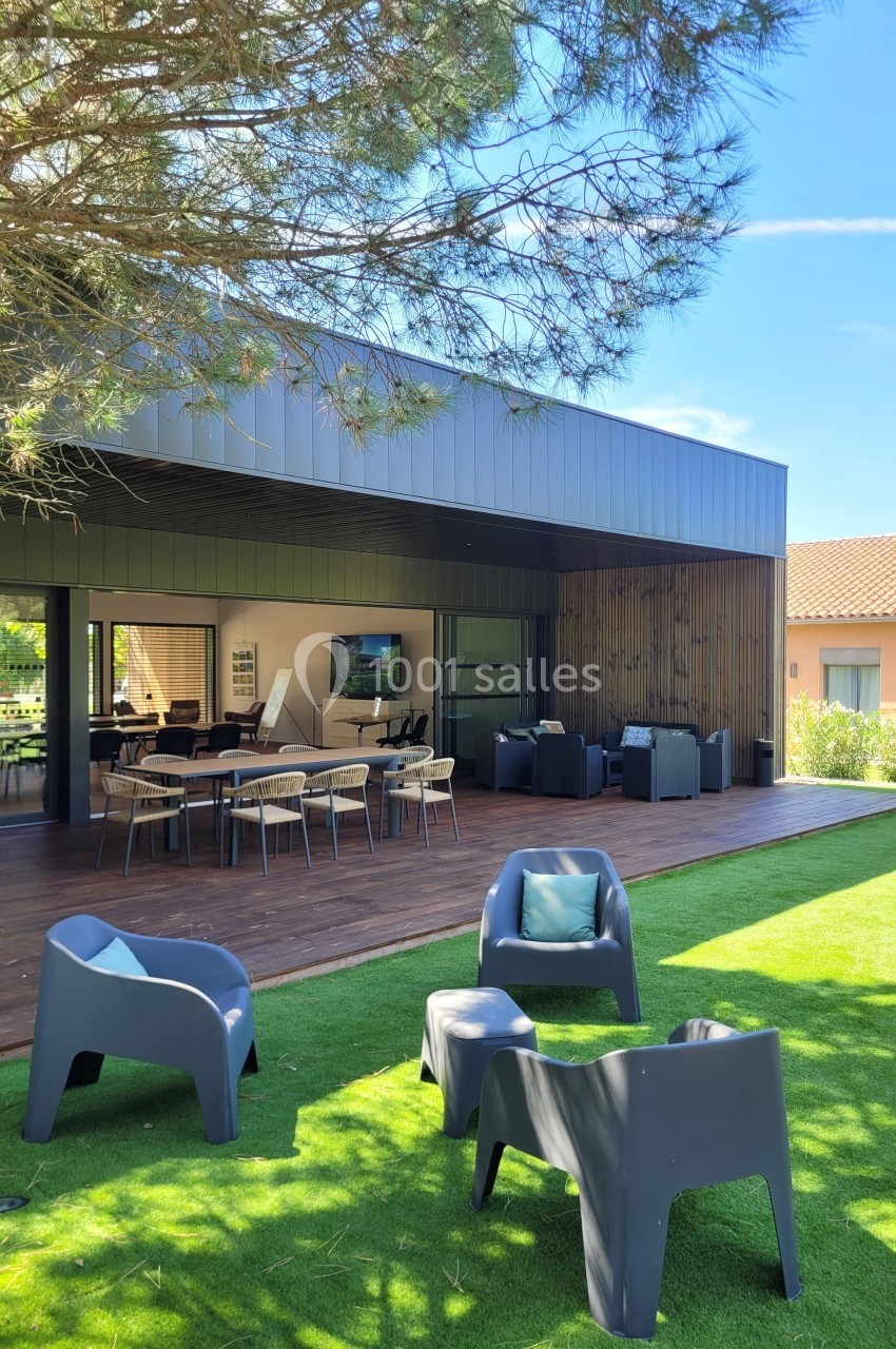 Terrasse moderne avec mobilier de jardin, espace repas et salon extérieur, entourée de pelouse et d'arbres.