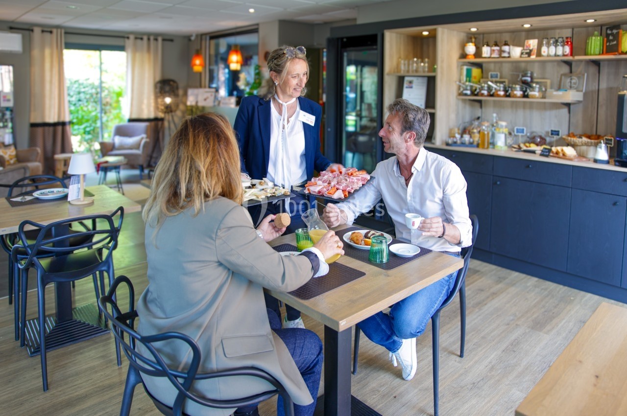 Une serveuse apporte des assiettes de nourriture à deux clients assis dans un café lumineux et moderne.