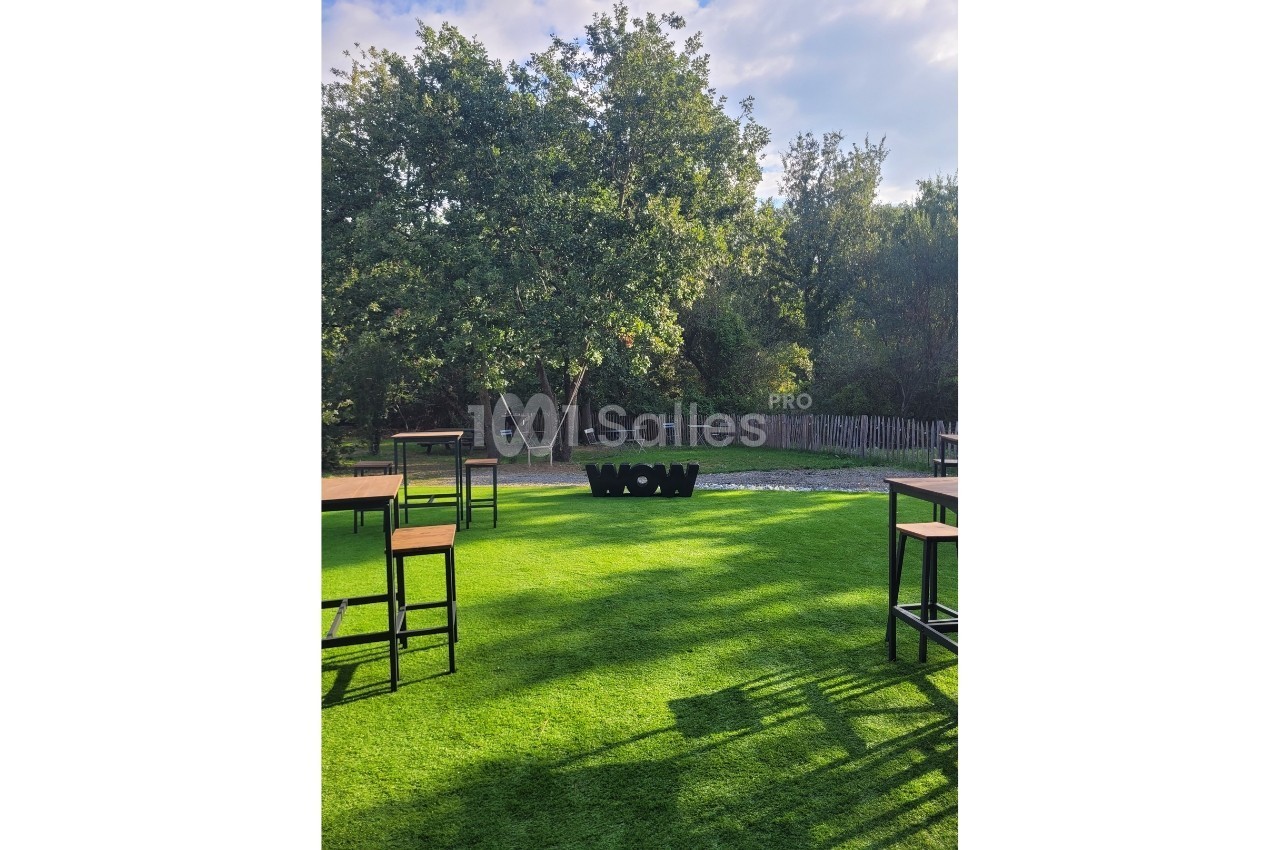 Tables hautes disposées sur une pelouse verte, avec des arbres en arrière-plan et le mot ’WOW’ en lettres noires.