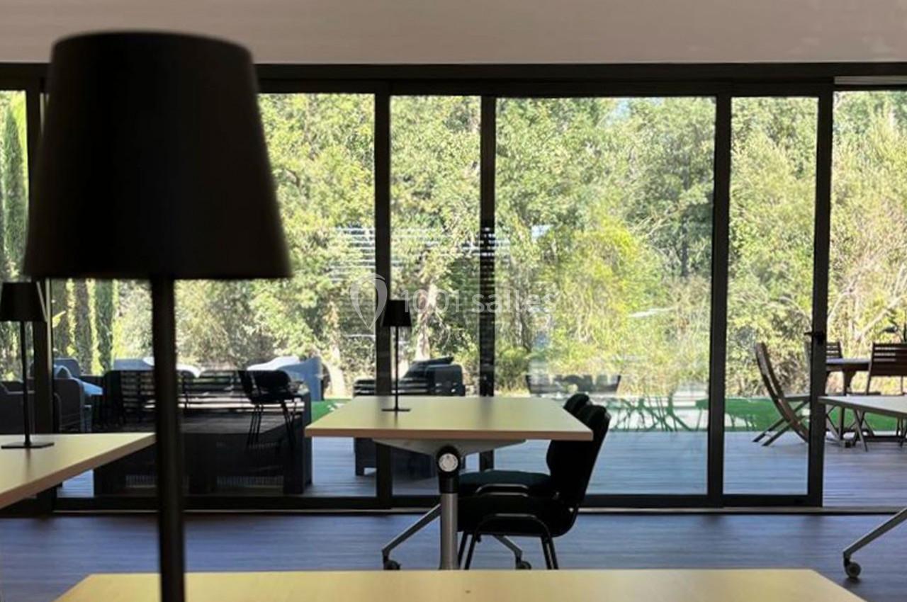 Salle lumineuse avec grandes baies vitrées donnant sur une terrasse et un espace extérieur verdoyant.