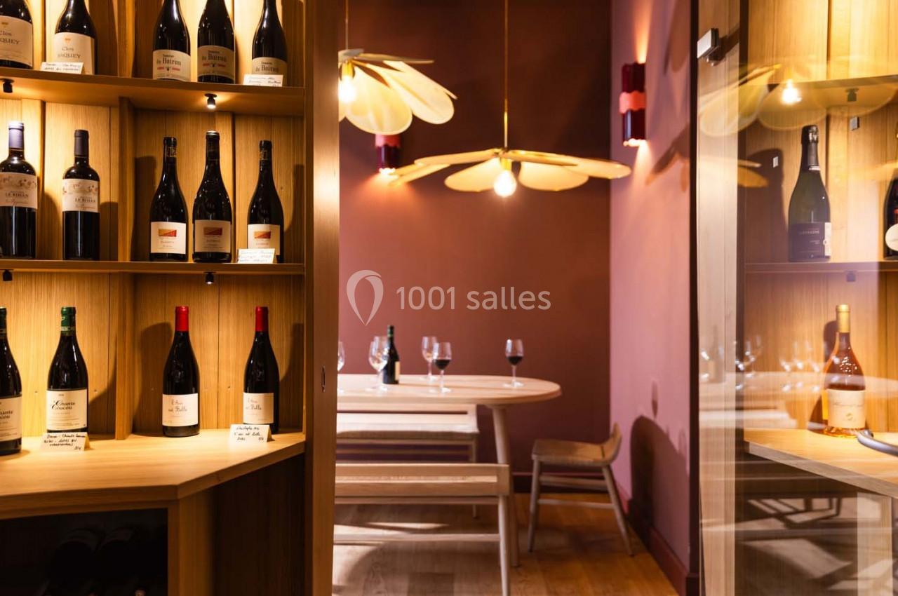 Cave à vin avec étagères de bouteilles éclairées et table dressée avec verres dans un espace chaleureux.