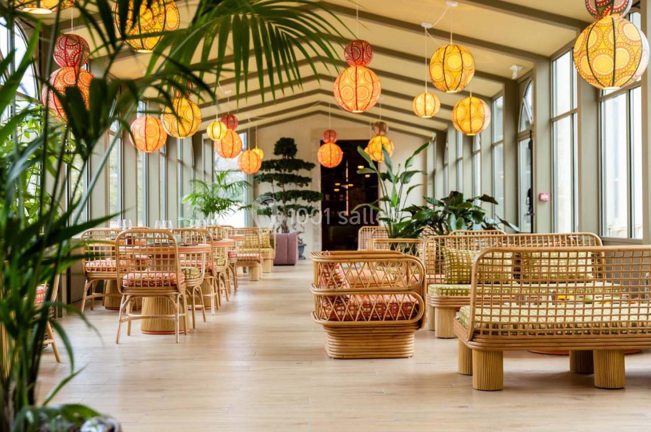 Salle lumineuse avec mobilier en rotin, plantes vertes et lampes suspendues aux motifs colorés.