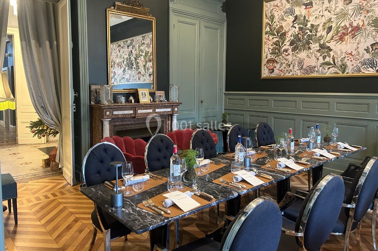 Salle à manger élégante avec une grande table dressée, chaises noires, cheminée en marbre et décor mural floral.