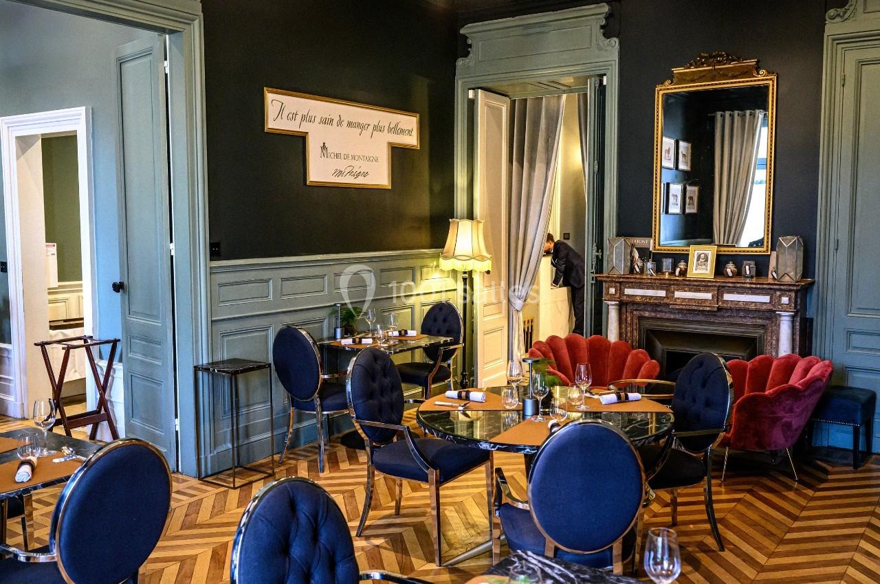 Salle de restaurant élégante avec parquet en chevrons, mobilier raffiné et cheminée ornée d'un miroir doré.