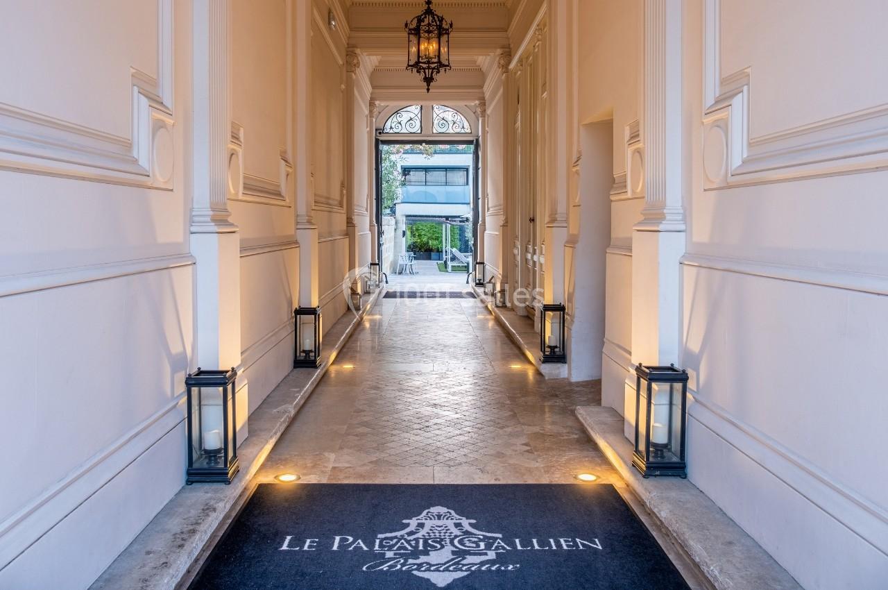 Entrée élégante d'un bâtiment avec sol en pierre, lanternes alignées et tapis marqué ’Le Palais Gallien Bordeaux’.