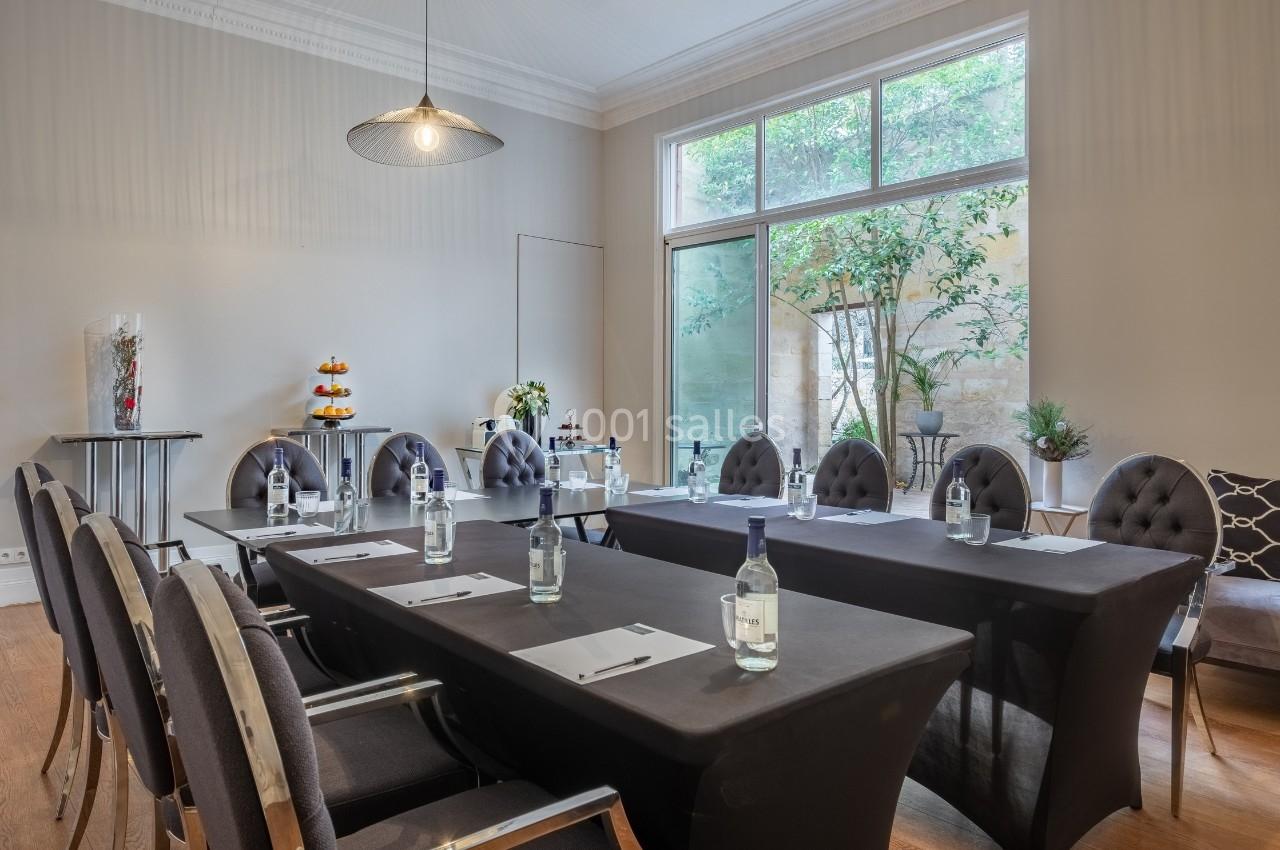 Salle de réunion lumineuse avec grandes fenêtres, tables disposées en U, chaises élégantes et bouteilles d'eau sur les…