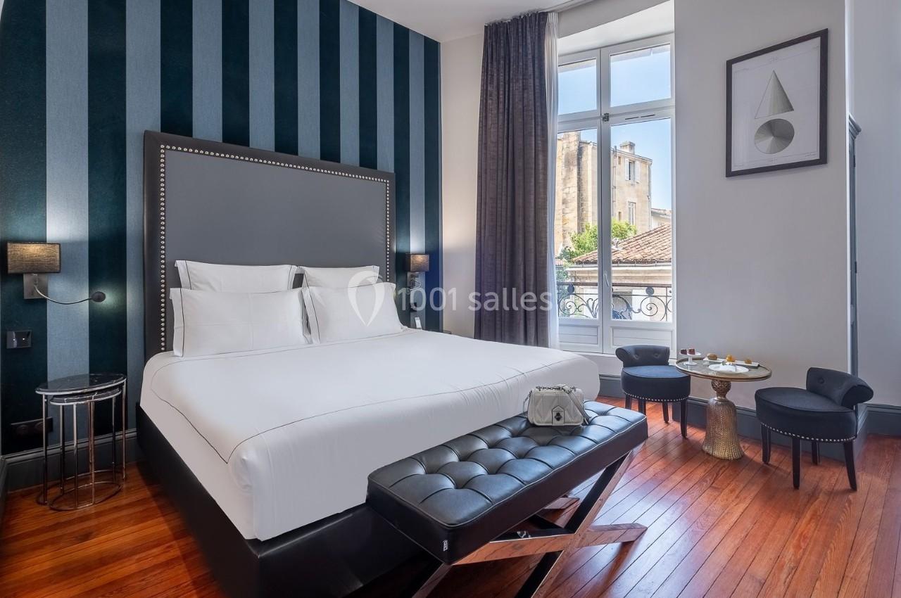 Chambre lumineuse avec lit double, parquet, mur à rayures, grande fenêtre et mobilier élégant.
