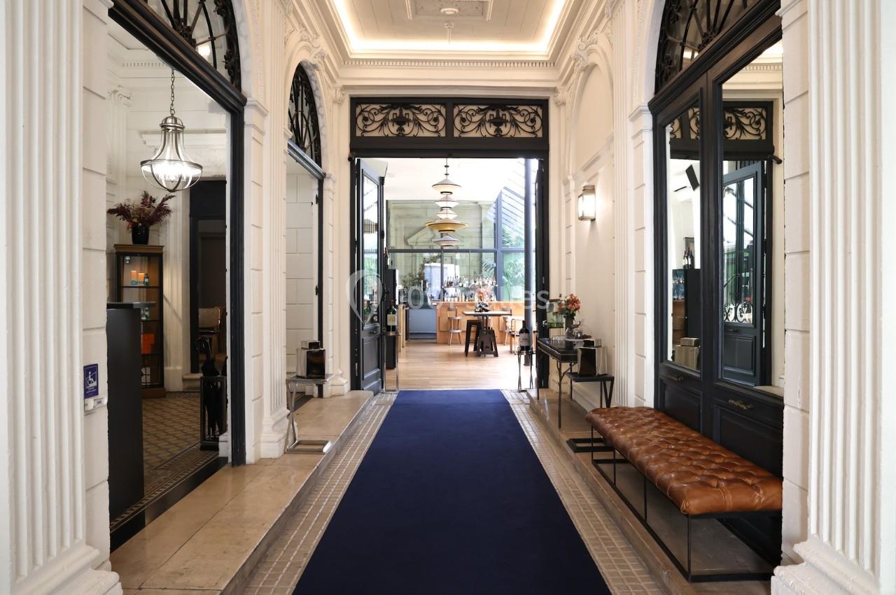 Entrée élégante avec tapis bleu, banc en cuir, murs ornés et vue sur un espace lumineux avec comptoir au fond.