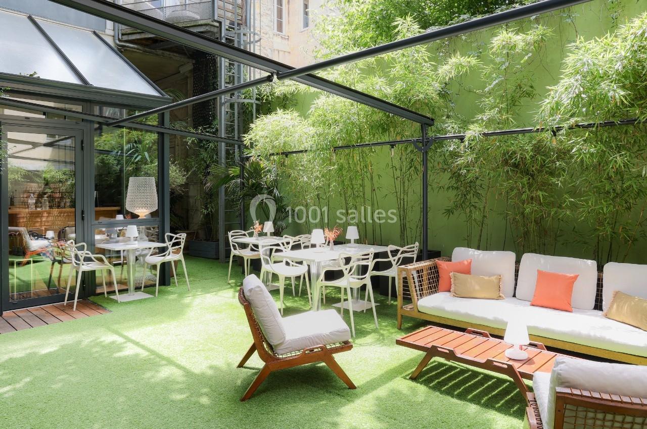Terrasse extérieure avec mobilier moderne, tables, chaises et canapés, entourée de bambous et d'un mur vert.
