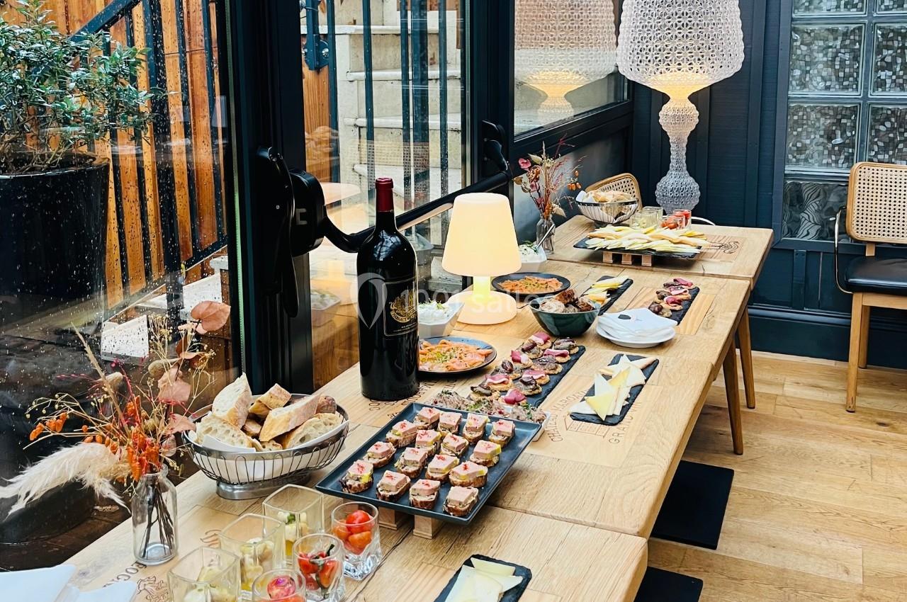 Table en bois garnie de plats variés, verrines, pains et bouteilles de vin, dans un espace lumineux avec une décoration…