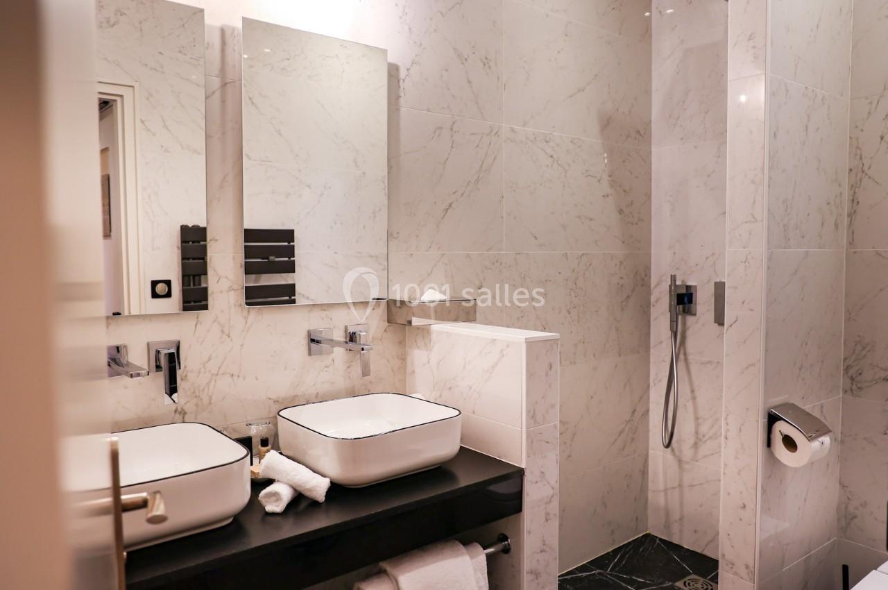 Salle de bain moderne avec deux vasques, murs en marbre clair, douche à l'italienne et accessoires minimalistes.