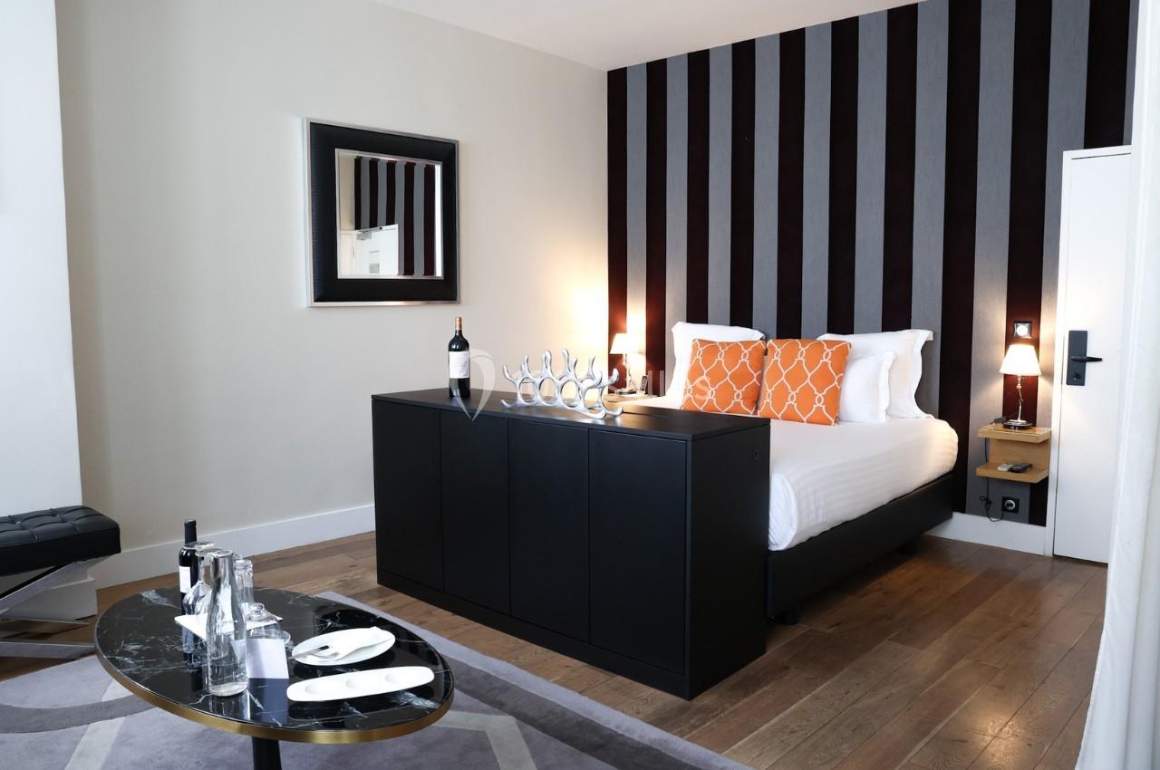 Chambre moderne avec lit double, décoration épurée, murs rayés, table basse avec plateau et bouteille de vin sur meuble.