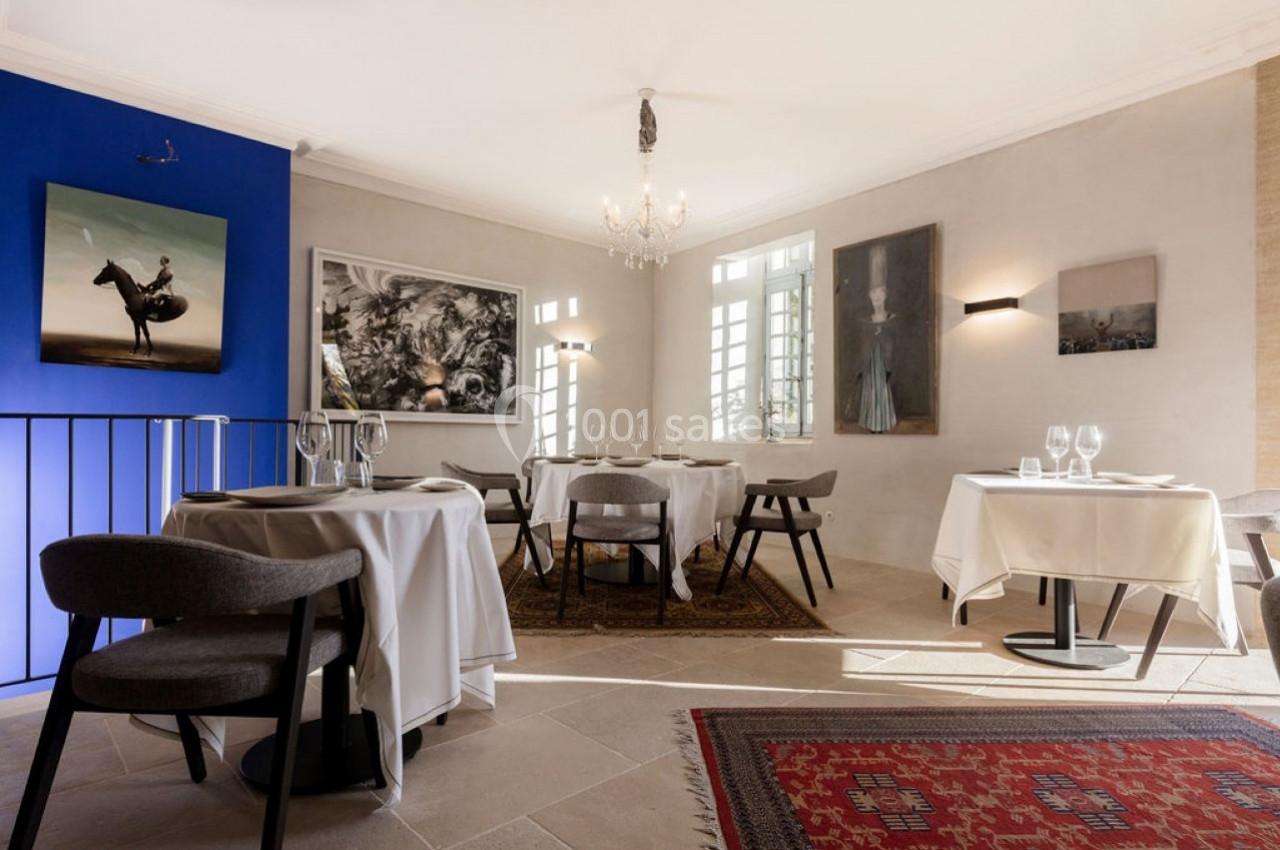 Salle de restaurant lumineuse avec tables dressées, murs décorés d'œuvres d'art et tapis au sol.